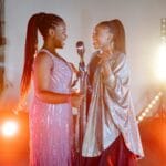 Dwie wokalistki śpiewają na scenie w kolorowych światłach koncertu