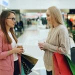 Dwie kobiety z kawą i torbami zakupów rozmawiają w galerii handlowej