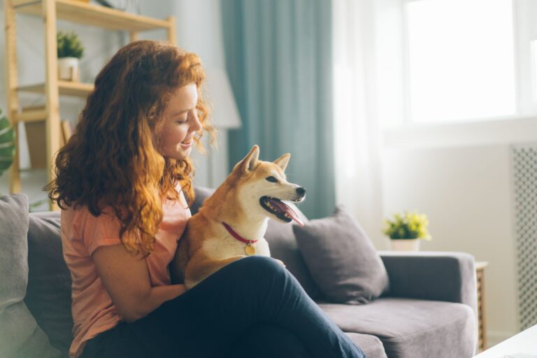 Rudowłosa kobieta siedzi na kanapie z psem rasy shiba inu